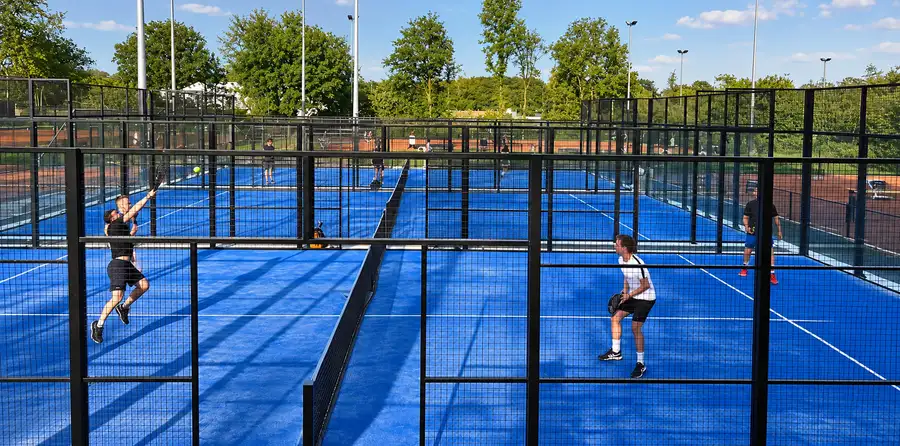 Spelers op de verlichte padelbanen van Racket & Fit Center in Borne, met de gravelbanen erachter