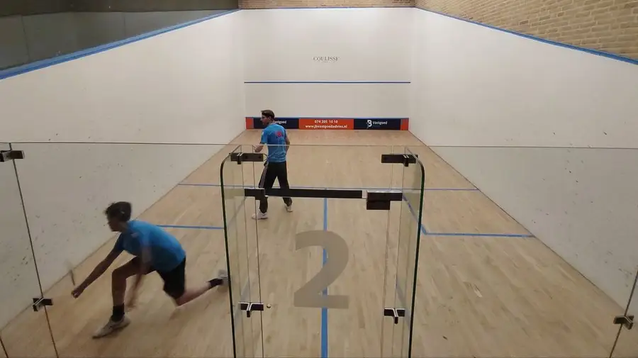 Twee spelers op een squashbaan met glazen achterwand bij Racket & Fit Center in Borne