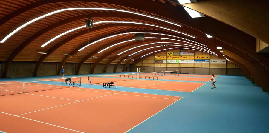 Indoor tennisbanen onder het houten tongewelf van Racket & Fit Center in Borne