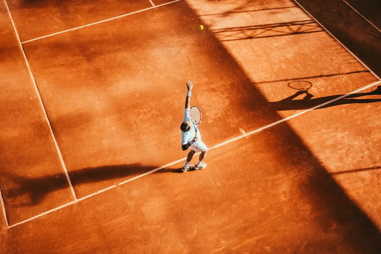 Tennisser slaat een opslag op een gravelbaan